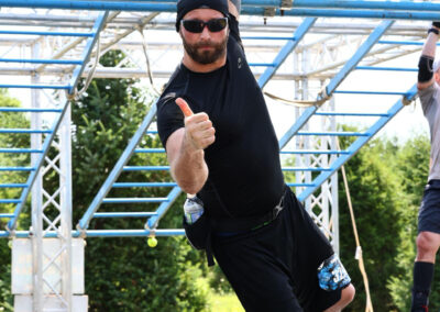 Photo of Sean McCormick hanging from climbing bars while giving the thumbs up during the Savage Race